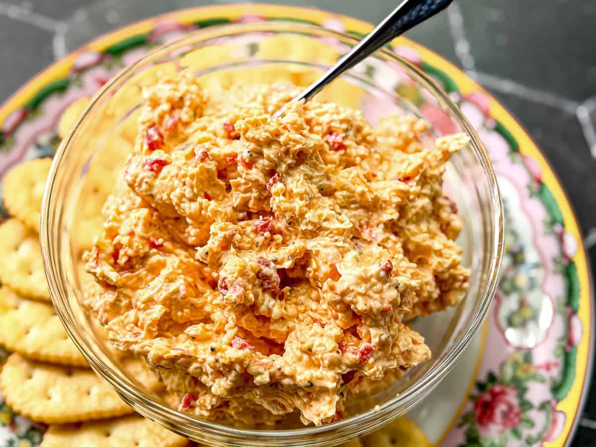 Pimento cheese in a glass bowl on a plate with crackers.