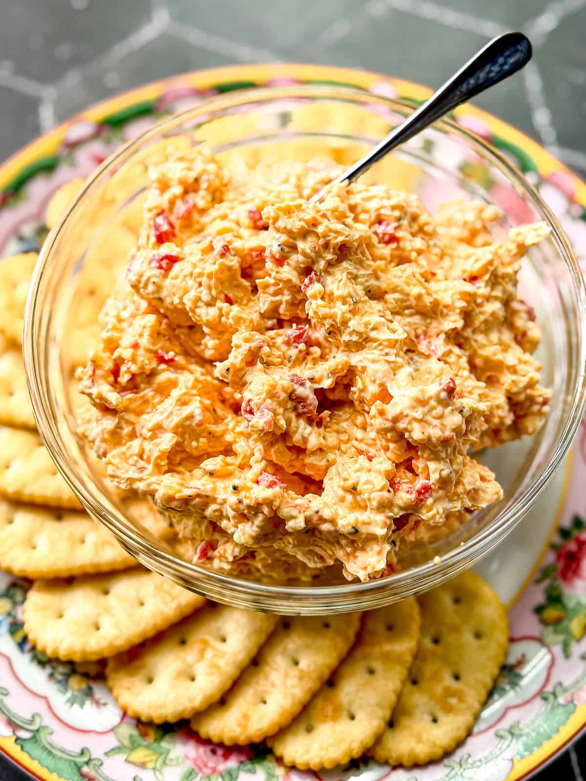 Pimento cheese in a glass bowl on a plate with crackers.