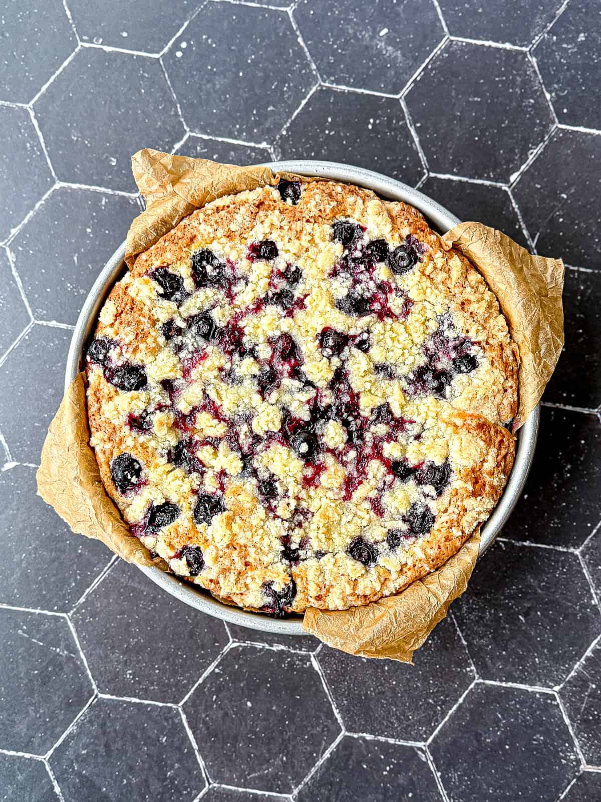 A baked blueberry topped French yogurt cake on a black background.