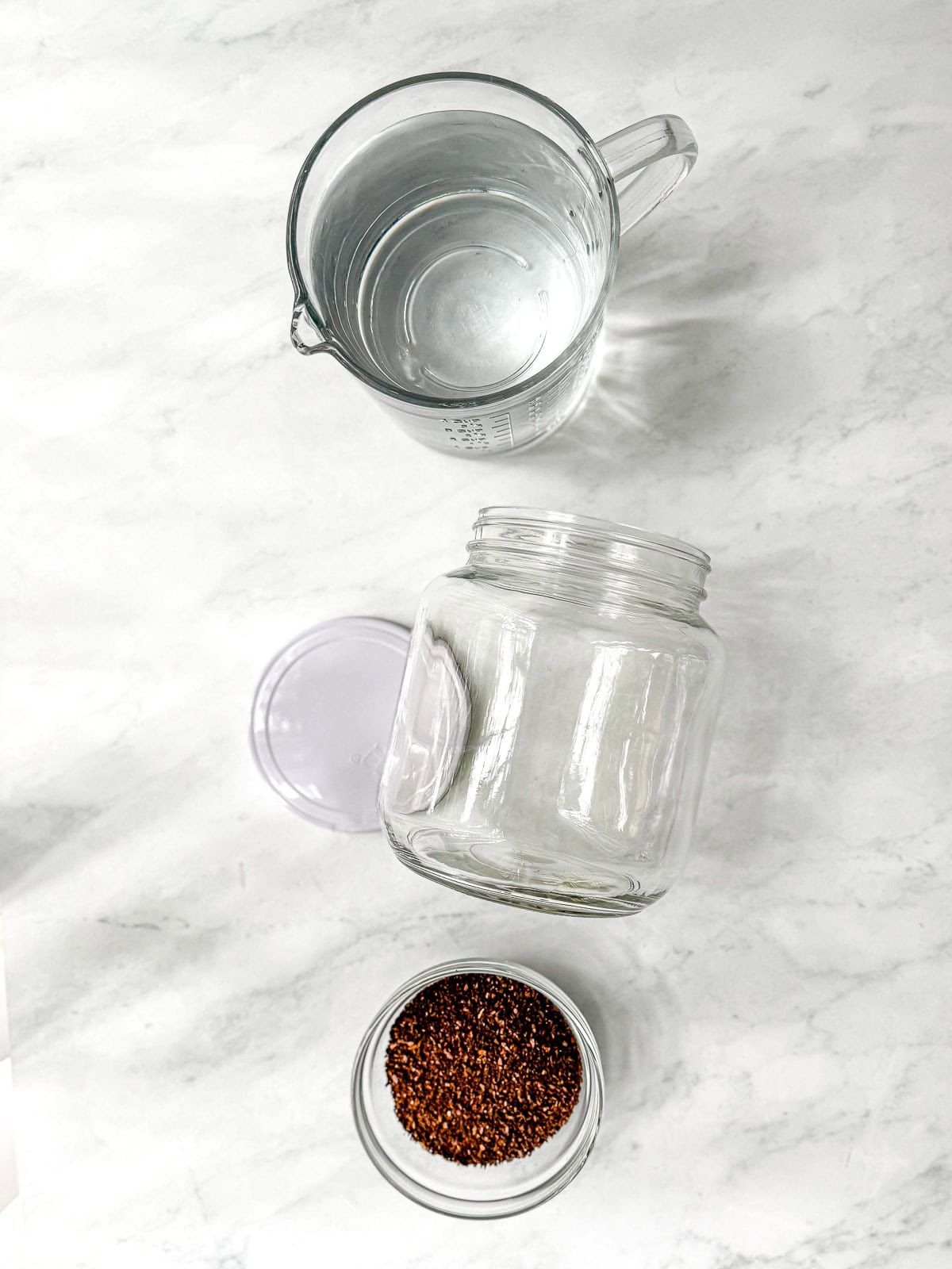 Water, a clear glass container, and a bowl of coarse ground coffee on a white background.