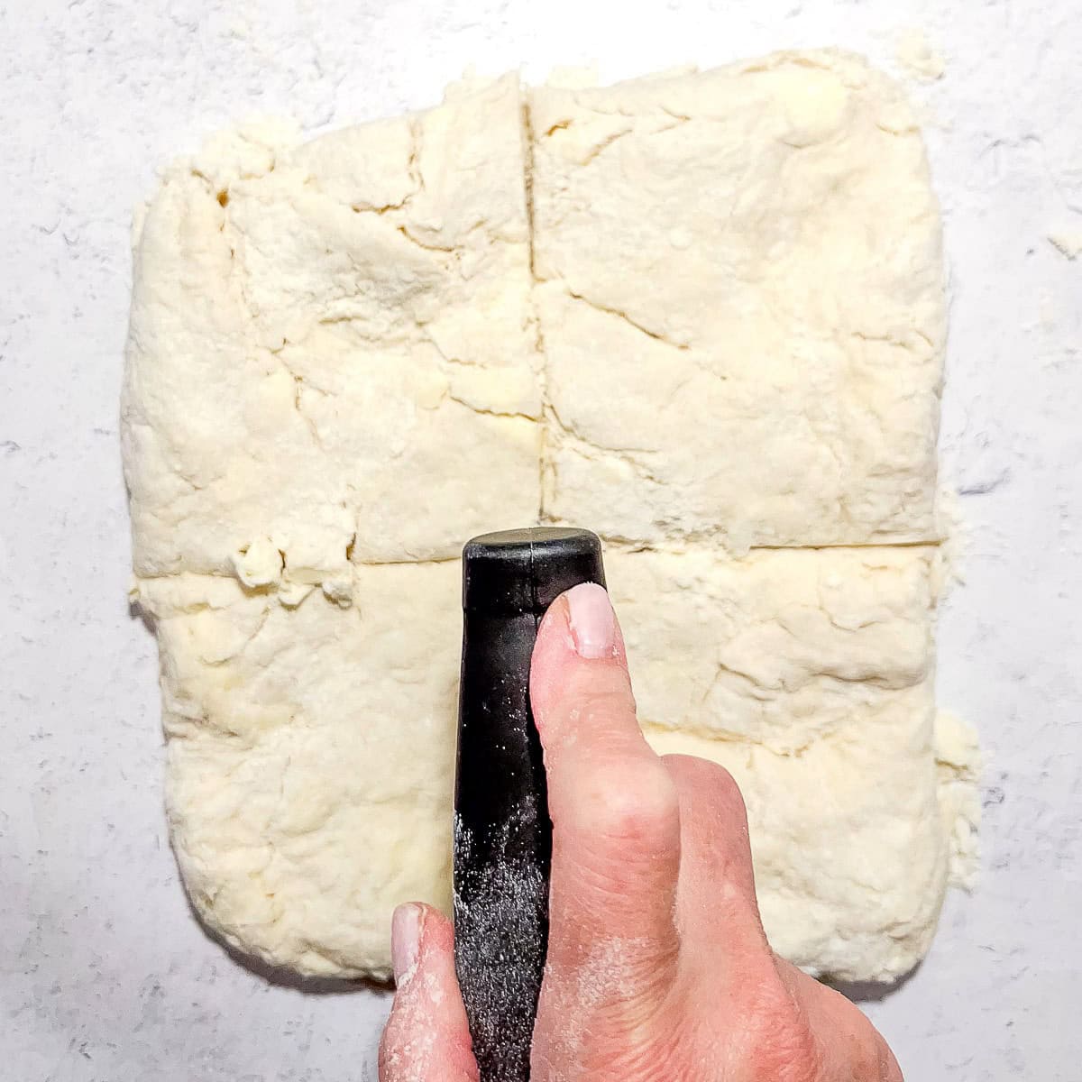 Using a bench scraper to cut biscuit dough in four pieces