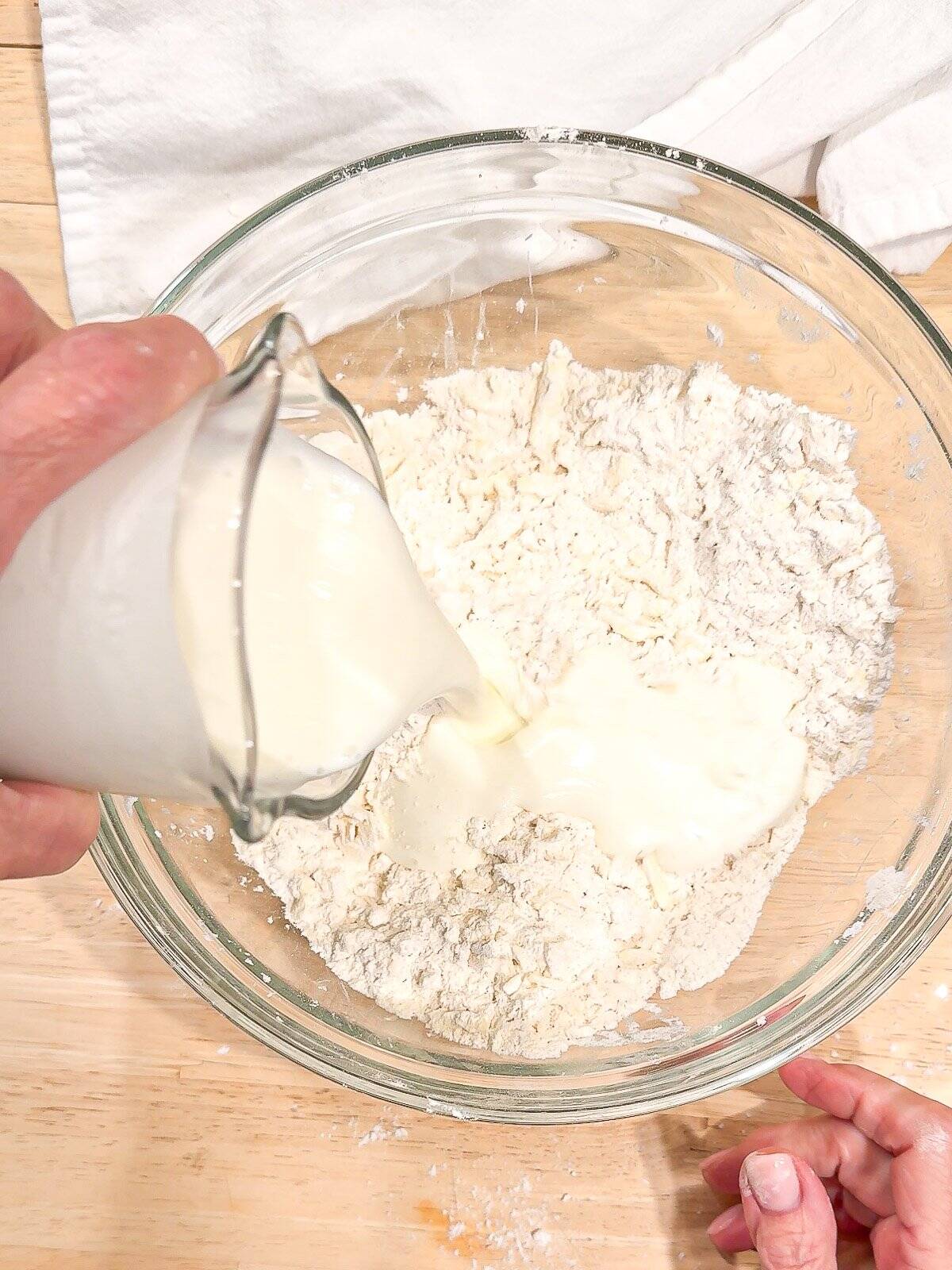 Adding buttermilk to dry ingredients in a glass bowl.