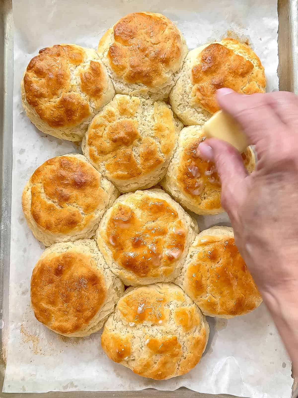 Rubbing softened butter on top of just baked three ingredient buttermilk biscuits.