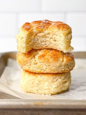 A stack of biscuits on a parchment paper lined sheet pan, the top one with a bite taken out.