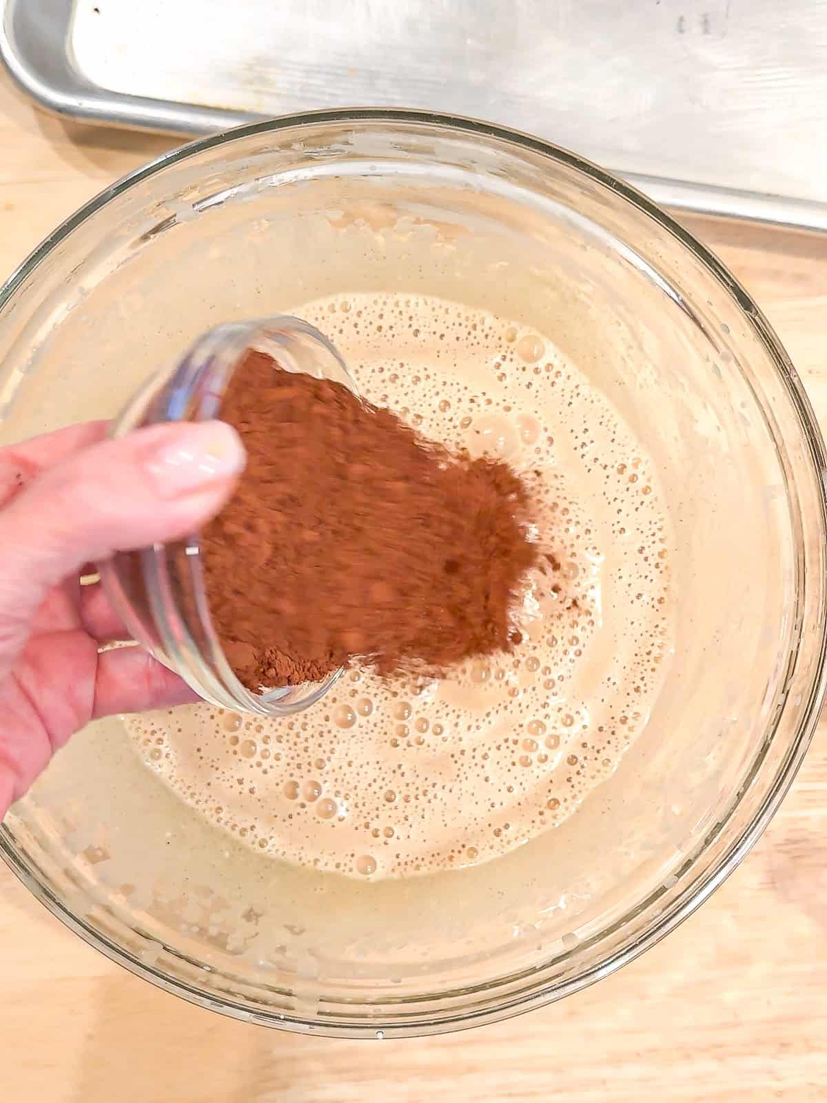 Adding cocoa powder to wet ingredients to make cake batter.
