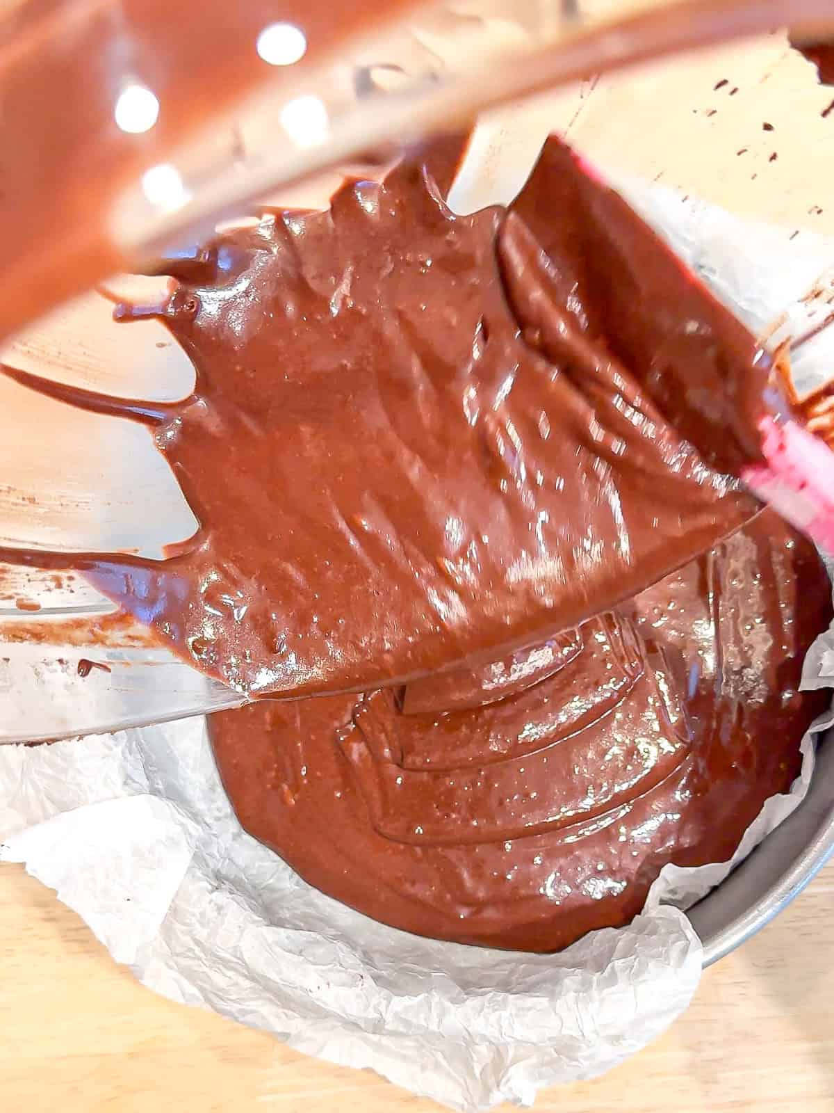 Pouring chocolate cake batter into a part of paper line cake pan.