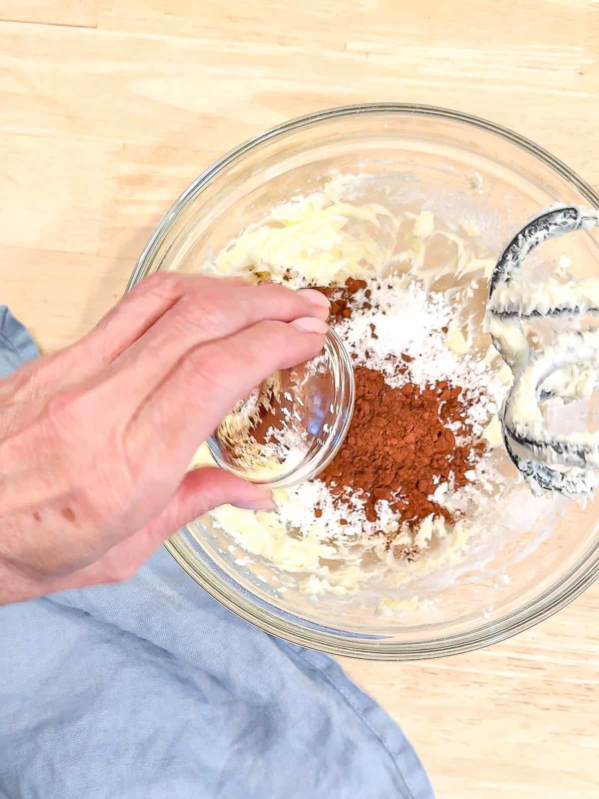 Adding cocoa powder to butter and powdered sugar to make buttercream.