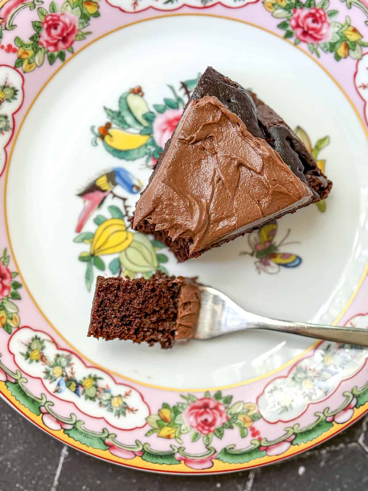 A slice of chocolate cake with double chocolate buttercream on a flowered plate.
