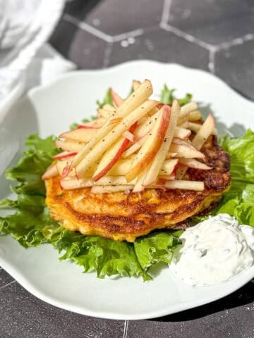 Corn fritter topped with apple slaw on a bed of lettuce.