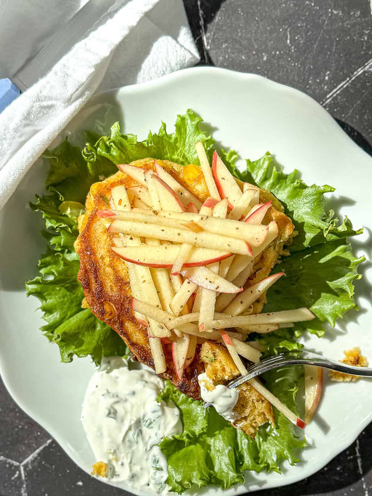 Corn fritter topped with apple slaw on a bed of lettuce.