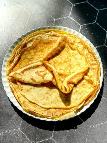 The stack of crêpes on a cream colored plate.