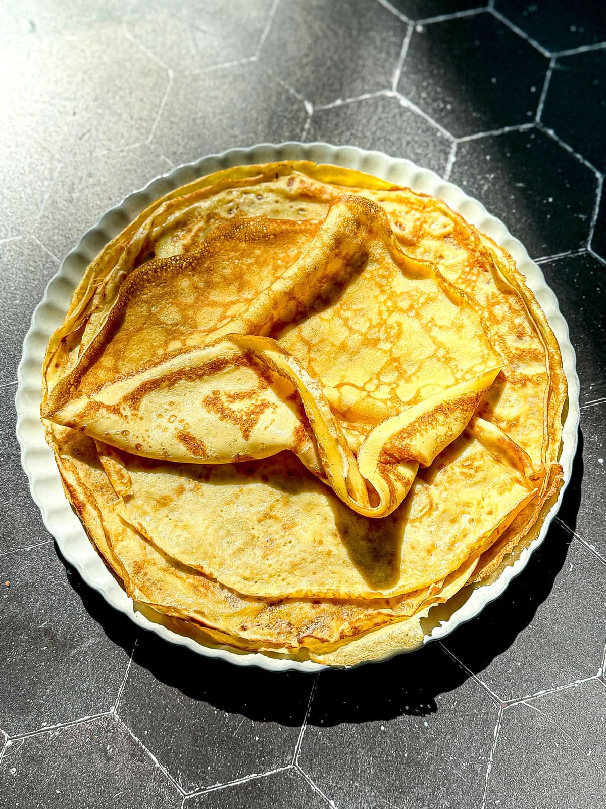 A stack of crêpes on a cream colored plate.