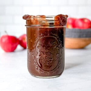 Pinterest image of a mason jar of apple butter in front of other apples.