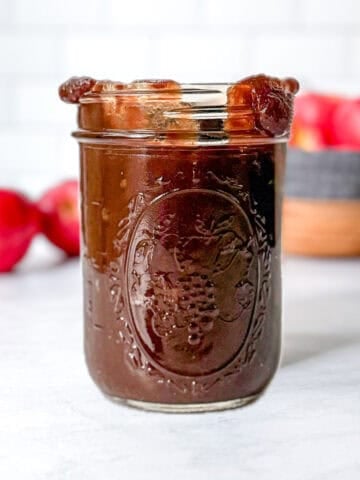 Pinterest image of a mason jar of apple butter in front of other apples.