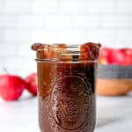 Pinterest image of a mason jar of apple butter in front of other apples.