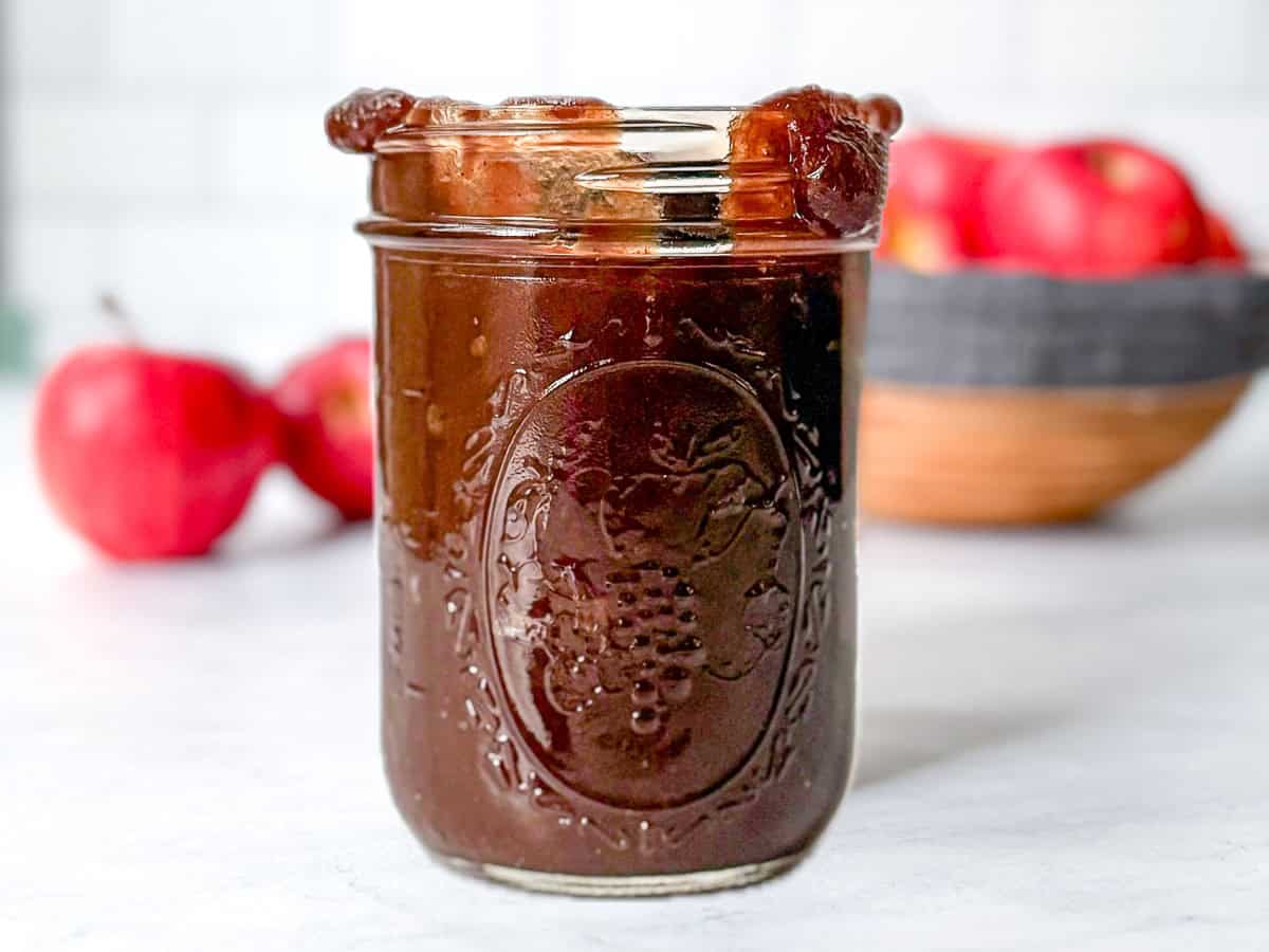 Pinterest image of a mason jar of apple butter in front of other apples.