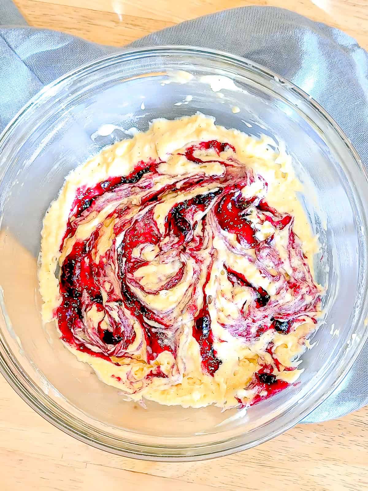 Blueberry jam swirled into donut batter in a glass bowl.