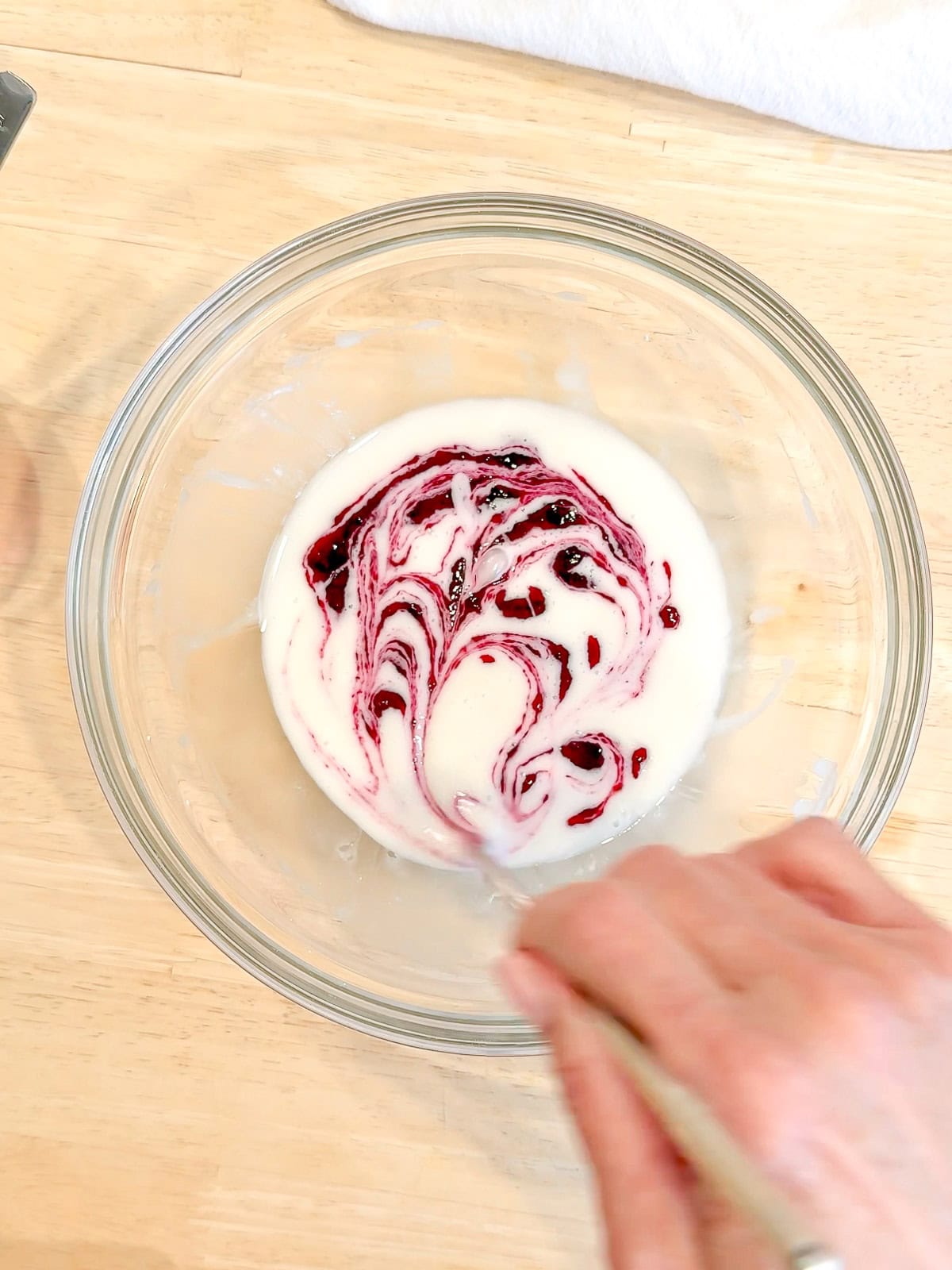 Swirling blueberry jam into glaze in a glass bowl.