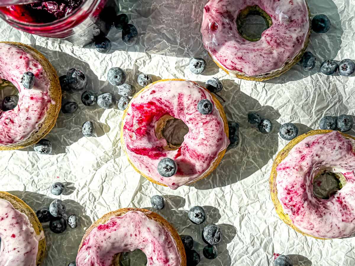 Blueberry swirl glazed donuts on parchment paper with blueberries scattered about.