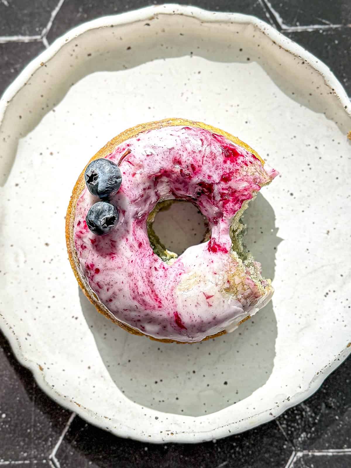 A glazed blueberry swirl donut on a white plate.