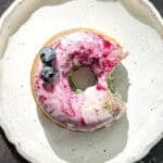 A glazed blueberry swirl donut on a white plate.