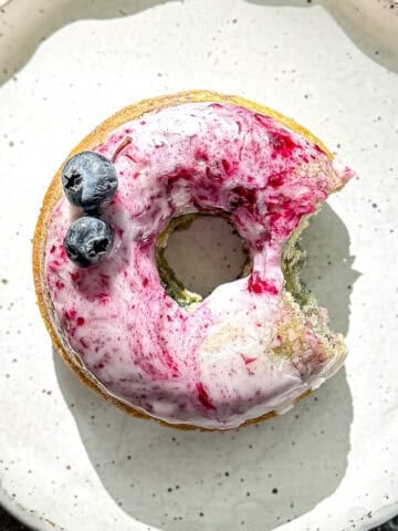 A glazed blueberry swirl donut on a white plate.