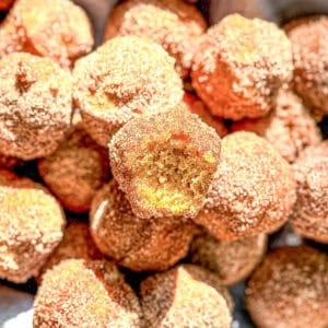 A pile of cinnamon cardamom mini donut muffins one with a bite taken out.