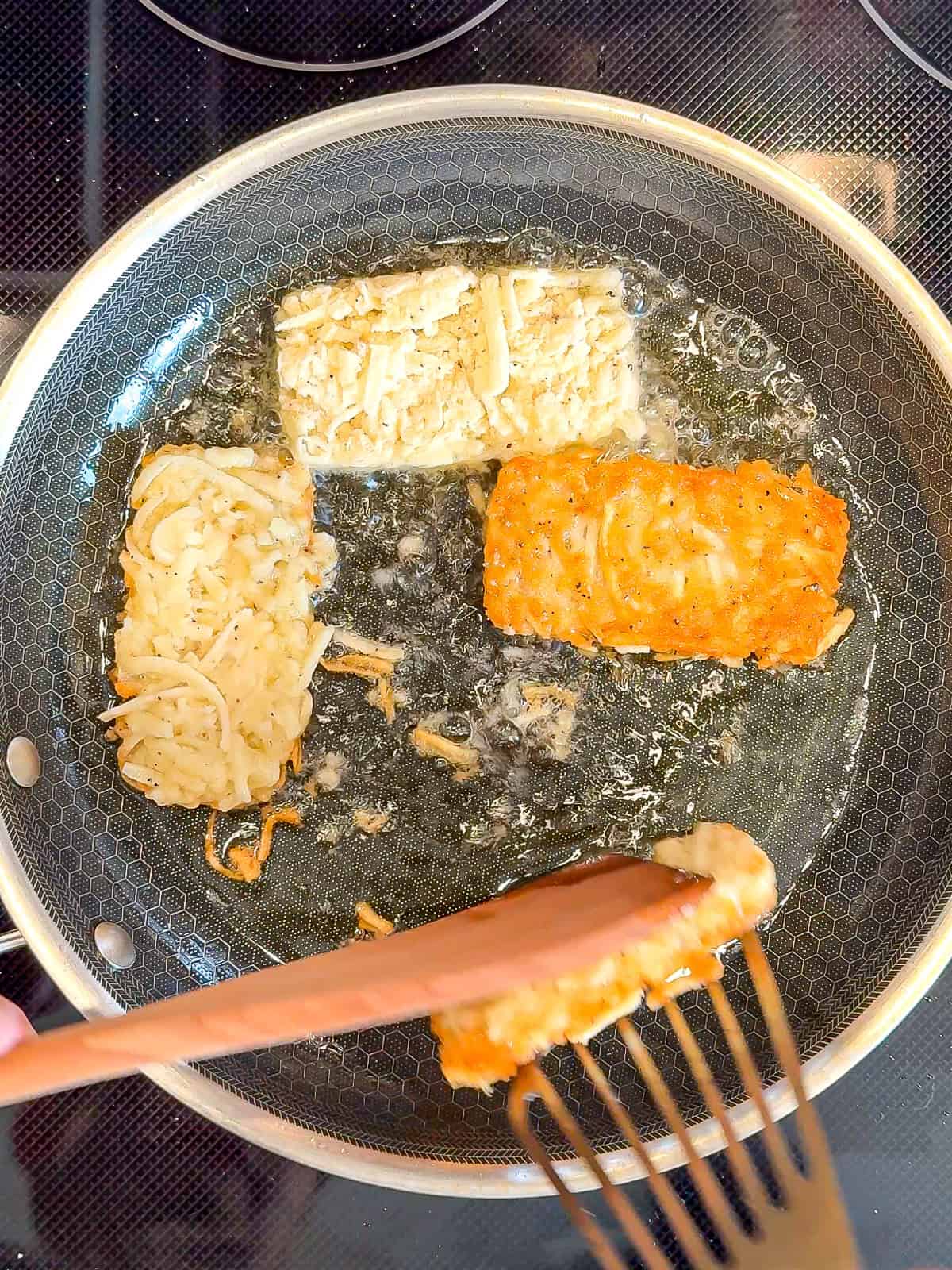 Using two spatulas to flip hash browns in a pan.