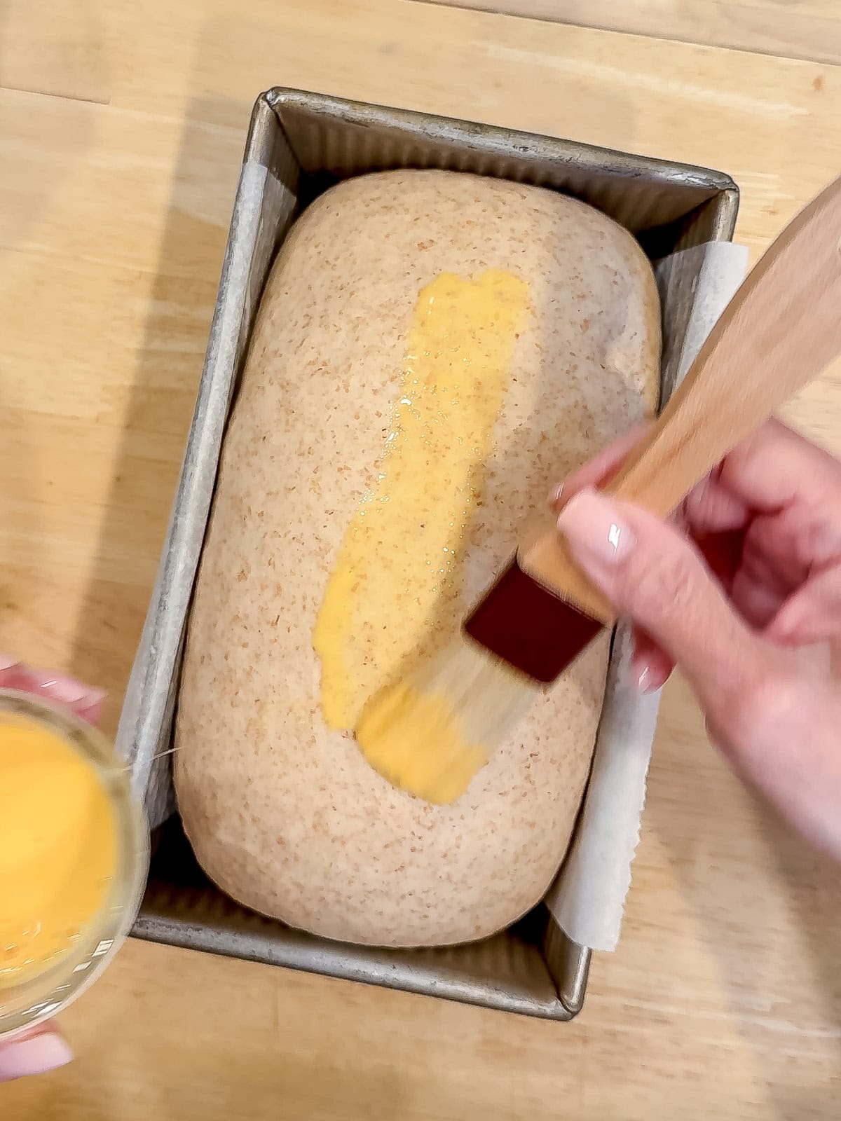 Brushing an egg wash on a fully rise loaf of wheat bread.