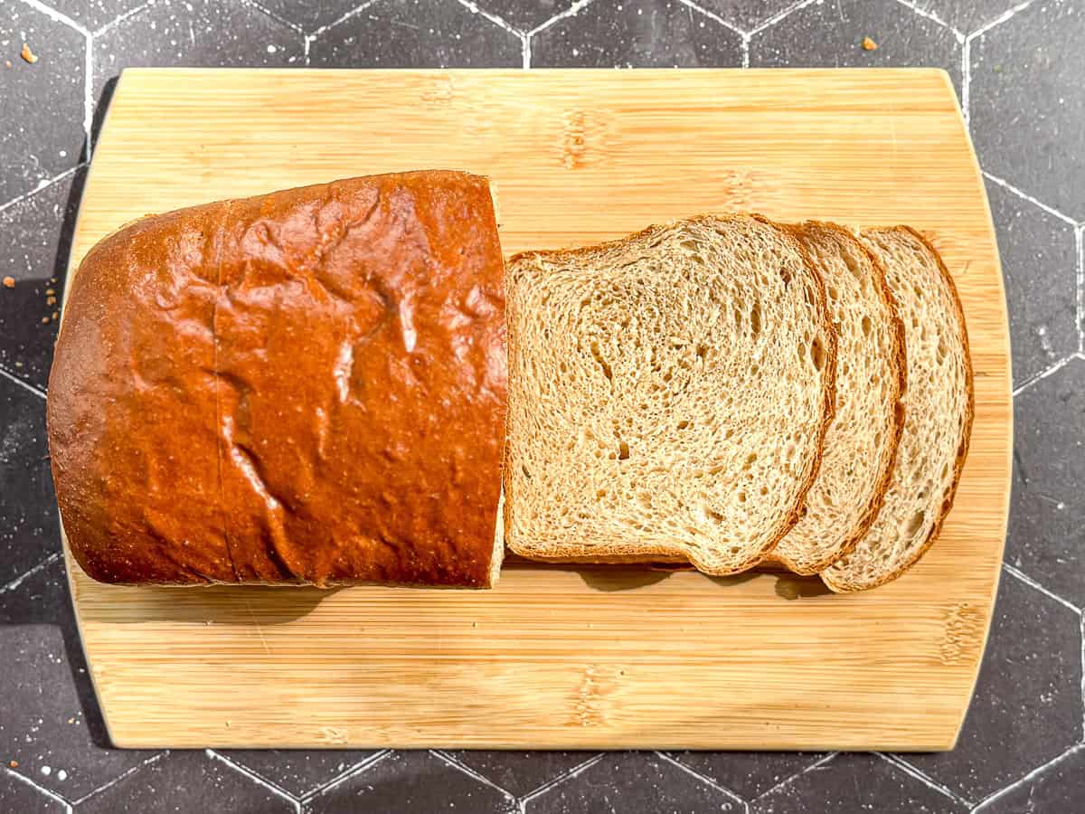 A sliced loaf of honey wheat bread on a wooden cutting board.