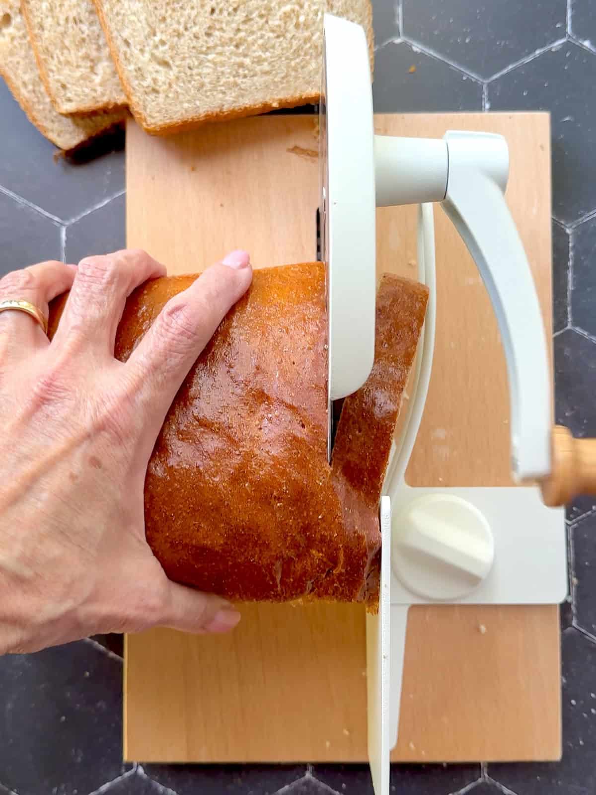 Slicing honey whole wheat bread with a manual crank slicer.