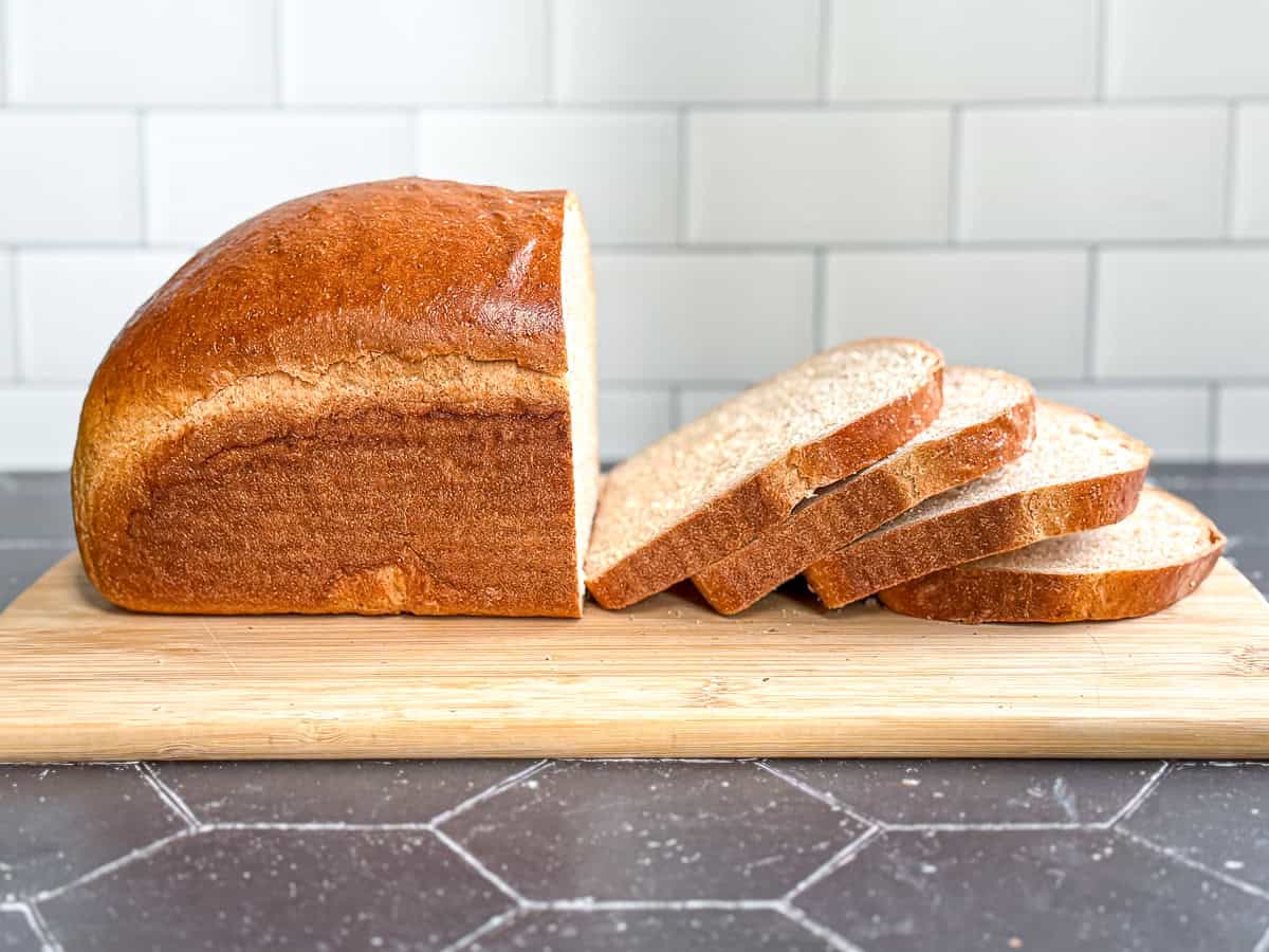 A sliced loaf of honey wheat bread on a wooden cutting board.
