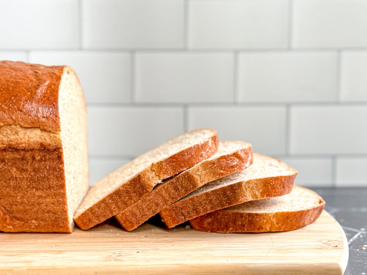 A sliced loaf of honey wheat bread on a wooden cutting board.