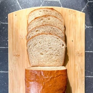 A sliced loaf of honey wheat bread on a wooden cutting board.