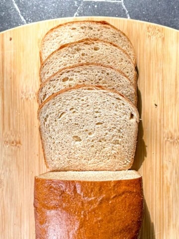 A sliced loaf of honey wheat bread on a wooden cutting board.