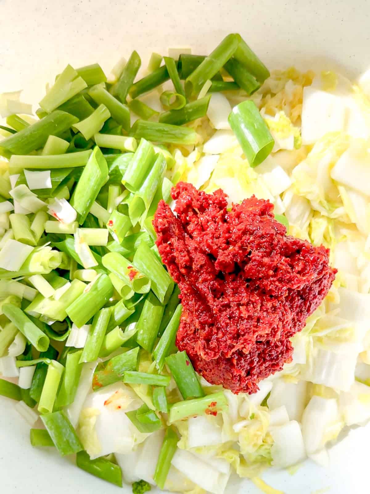 Adding kimchi paste to brined cabbage and green onion.