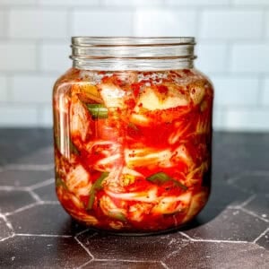 A jar of kimchi on a black background with a white backdrop.