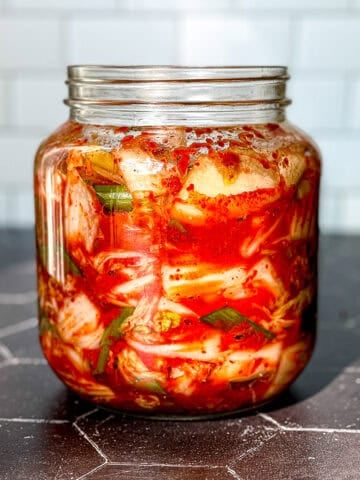 A jar of kimchi on a black background with a white backdrop.