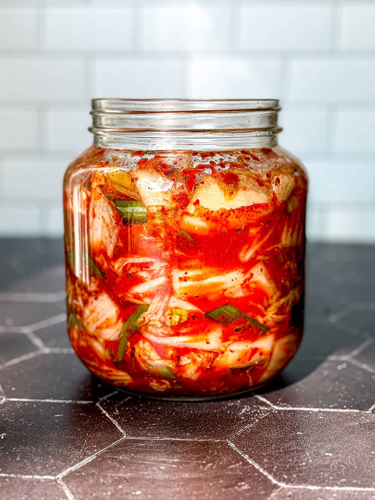 A jar of kimchi on a black background with a white backdrop.