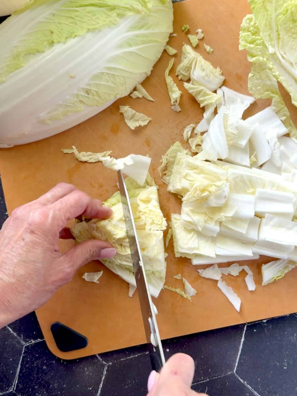 Chopping Napa cabbage on a brown cutting board.