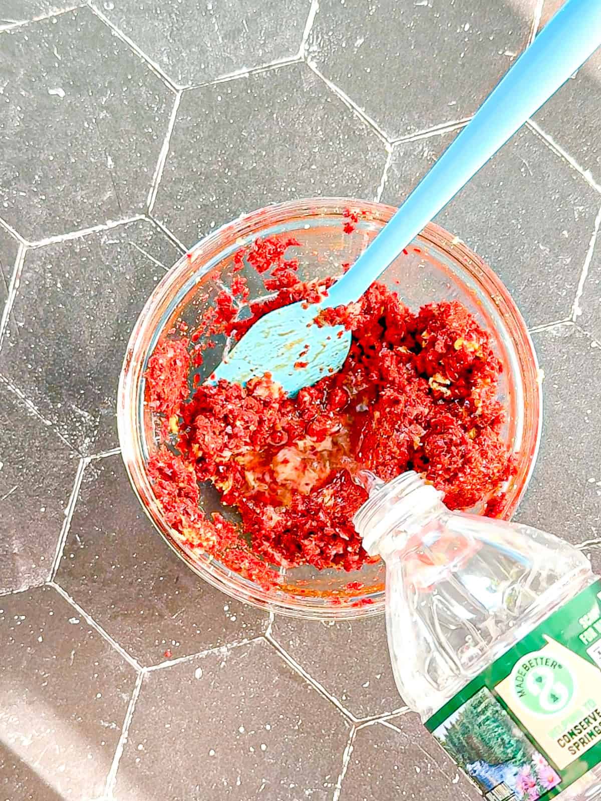 Adding bottled water to other ingredients to make kimchi paste in a glass bowl.