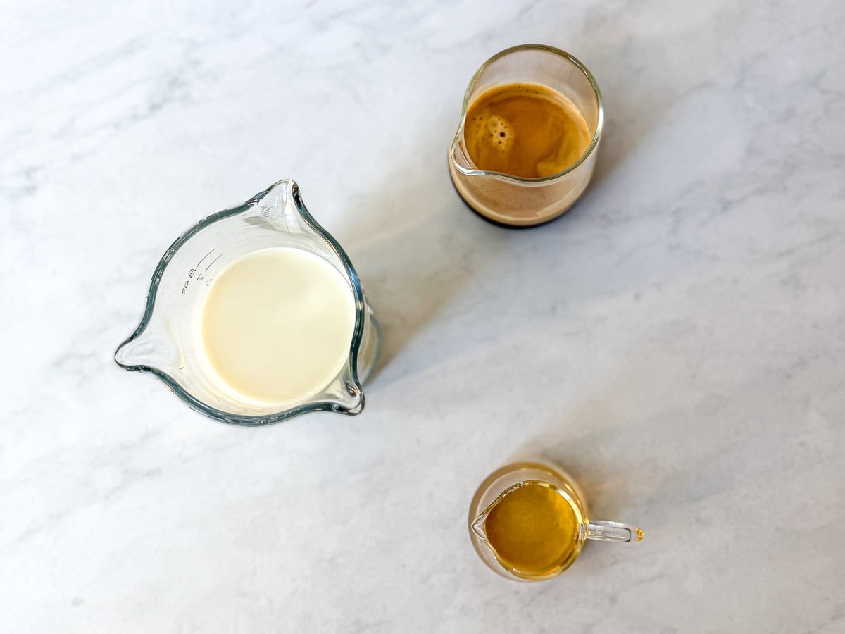 Milk, hot espresso, and vanilla simple syrup and small containers on a white backdrop.