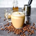 A mug of vanilla simple syrup in the middle of spilled coffee beans.