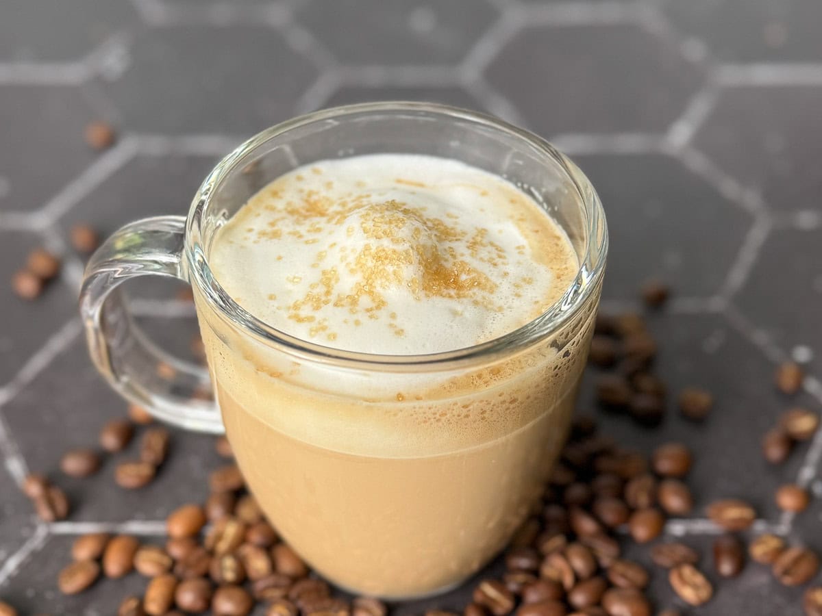 Glass mug holding a homemade vanilla latte sprinkled with vanilla sugar.