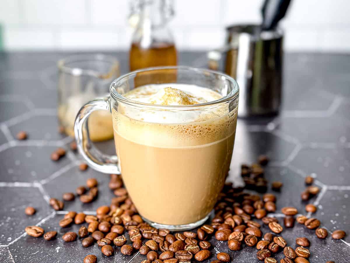 A mug of vanilla simple syrup in the middle of spilled coffee beans.