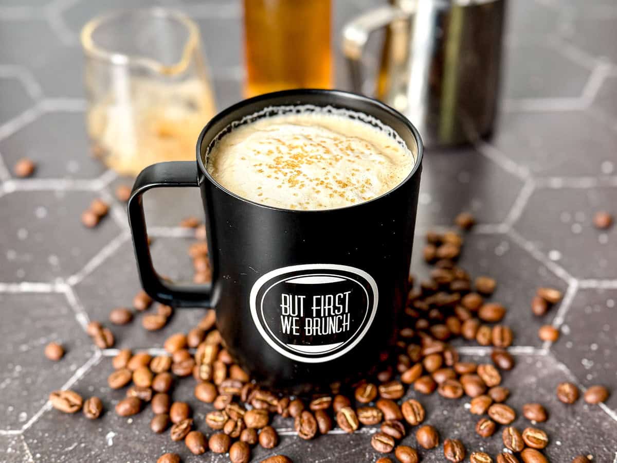 Vanilla latte in a black mug with the words but first we brunch on the front.