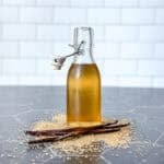 Pinterest image of a bottle of vanilla simple syrup on a black counter surrounded by sugar and vanilla bean pods.