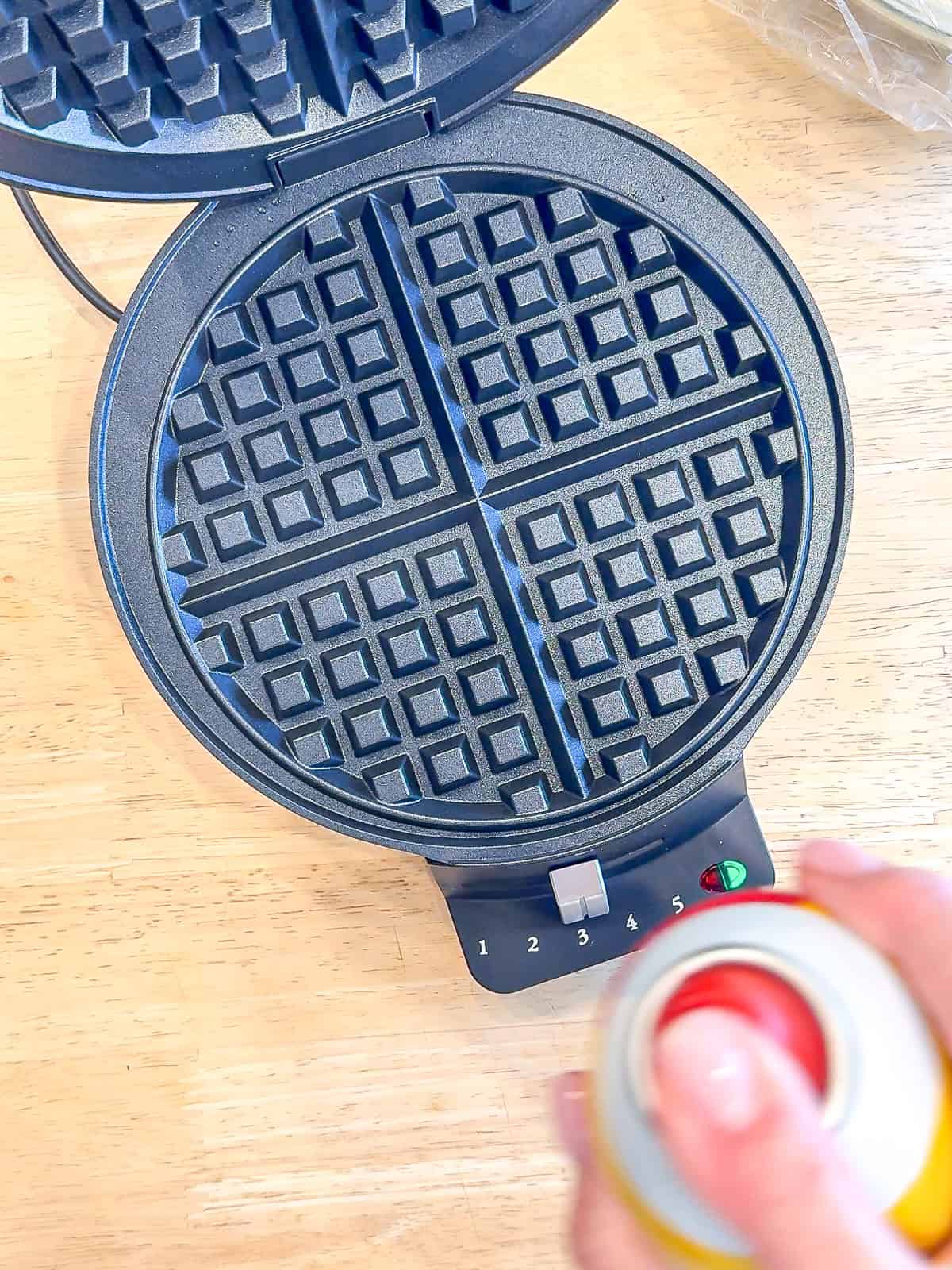 Spraying a waffle maker with nonstick spray.