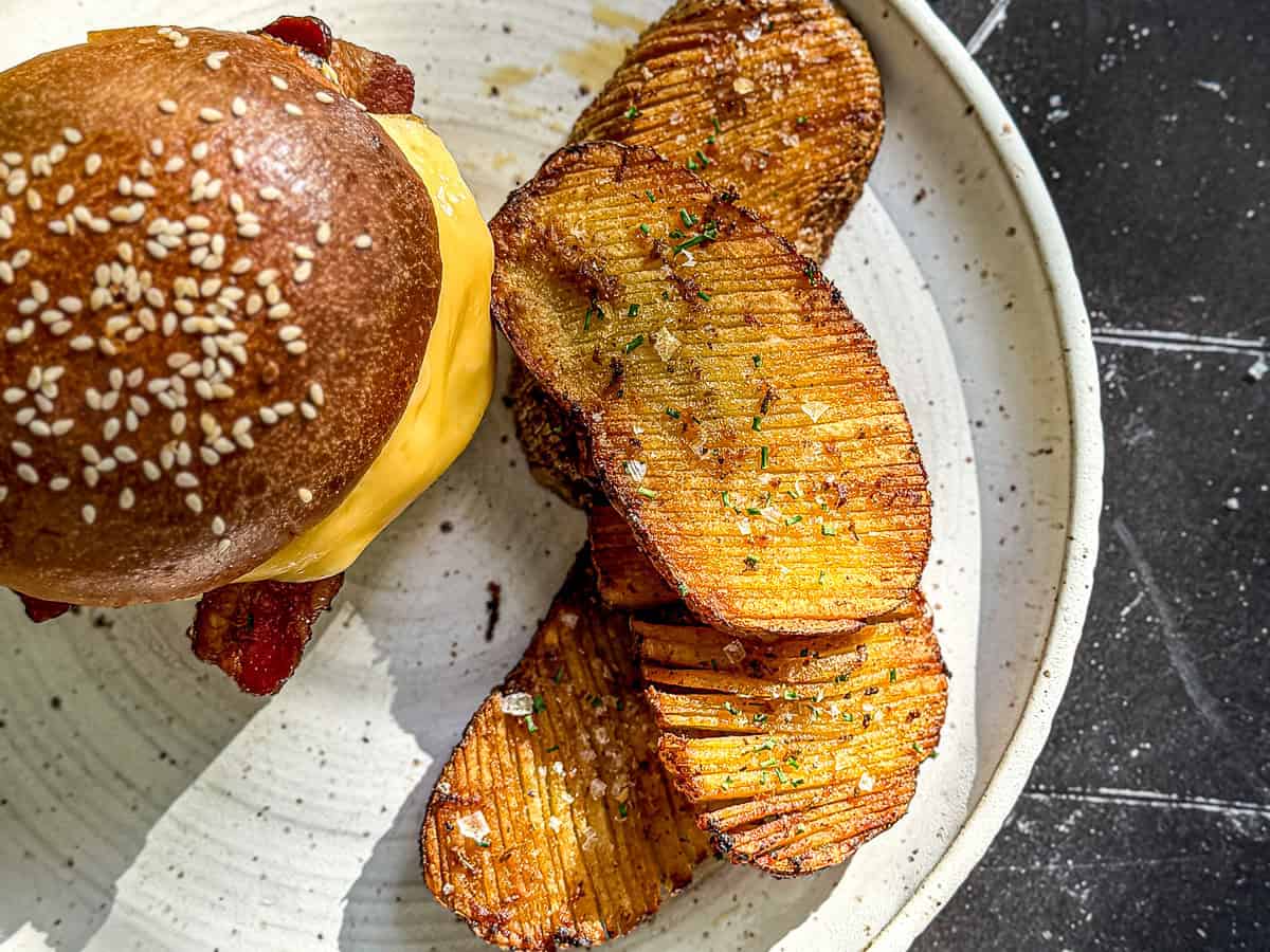 Crispy accordion potatoes next to a breakfast sandwich on a white plate.