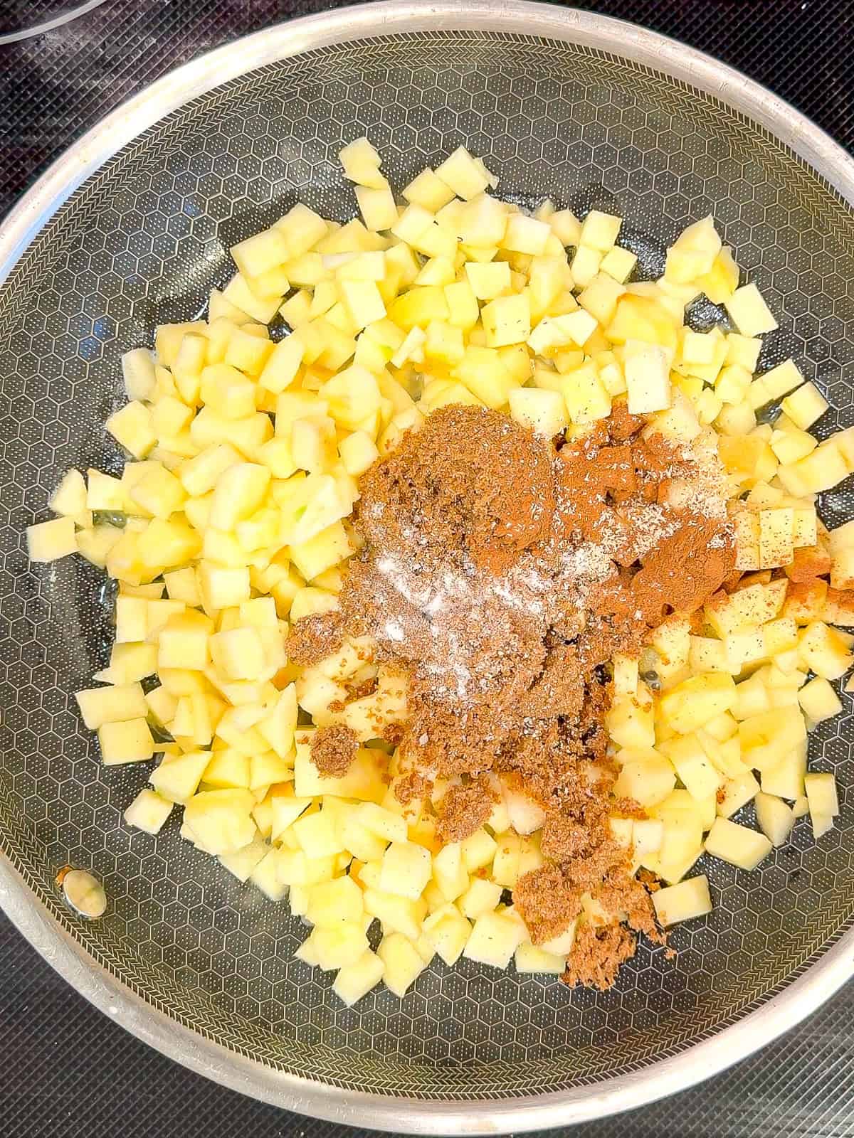 Diced apples, brown sugar, cinnamon, and a pinch of salt in a black pan.